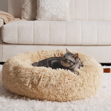 Load image into Gallery viewer, A cosy cat lying in a plush, beige round anxiety relieving cat bed on a soft white rug